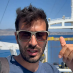 Persona che gesticola sul ponte di un traghetto con lo Stretto di Messina sullo sfondo