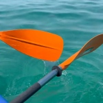 Due pale di remo arancioni su un kayak che sfiorano il mare turchese
