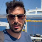 persona con occhiali da sole sul ponte di un traghetto con auto e mare sullo sfondo