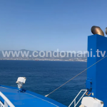 vista del mare e della scia dello stretto dalla prua del traghetto con camino blu e costa in lontananza