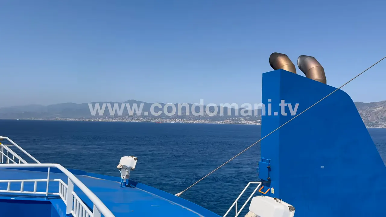 vista del mare e della scia dello stretto dalla prua del traghetto con camino blu e costa in lontananza