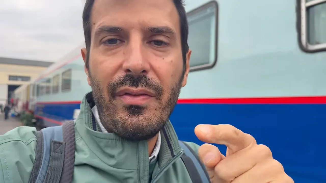 Persona che indica con il dito verso la fotocamera, con un treno storico sullo sfondo